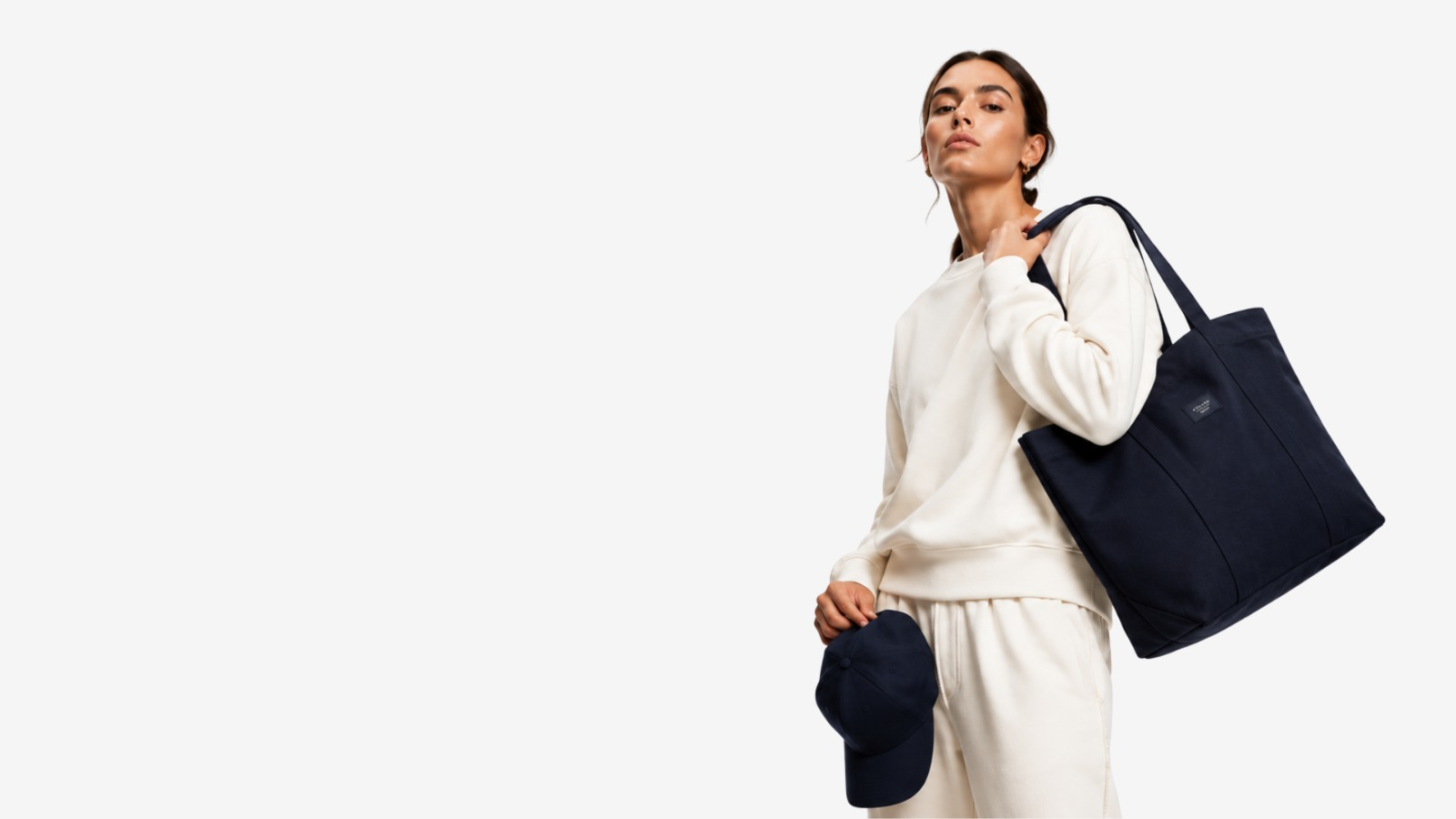 Model carrying a custom branded tote bag and cap with cream sweats by Safir Wear